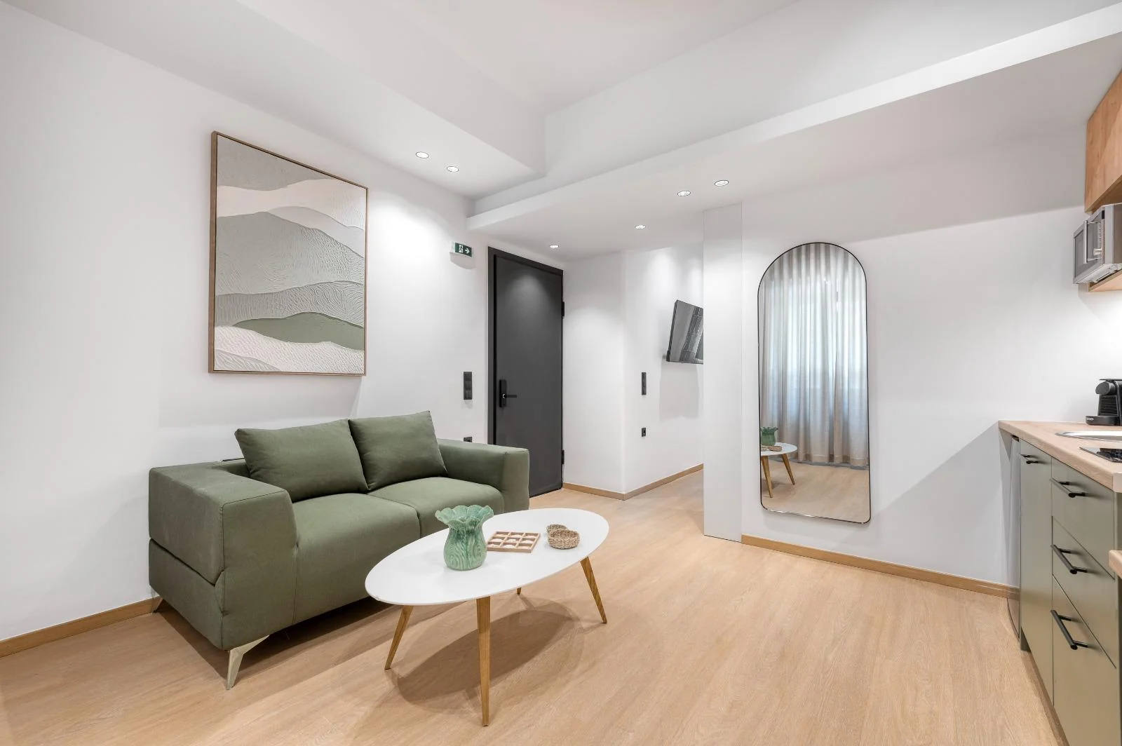 Apartment living area with green sofa, kitchenette and arched mirror at Dock 38